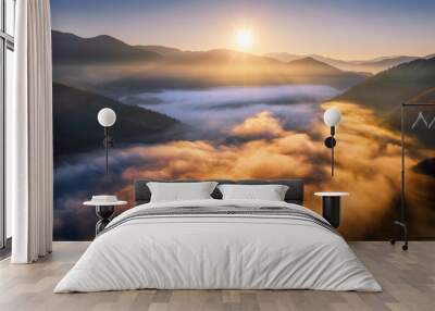 Mountains in low clouds at sunrise in autumn. Aerial view of mountain peak in fog in fall. Beautiful landscape with rocks, forest, sun, colorful sky. Top view of mountain valley in clouds. Foggy hills Wall mural