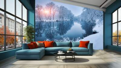 Winter forest on the river at sunset. Colorful landscape with snowy trees, frozen river with reflection in water. Seasonal. Snow covered trees, lake, sun and blue sky. Beautiful forest in snowy winter Wall mural