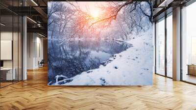 Winter forest on the river at sunset. Colorful landscape with snowy trees, frozen river with reflection in water. Seasonal. Winter trees, lake, sun and blue sky. Beautiful snowy winter in countryside Wall mural