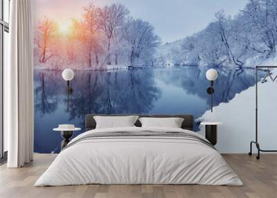 Winter forest on the river at sunset. Panoramic landscape with snowy trees, sun, beautiful frozen river with reflection in water. Seasonal. Winter trees, lake and blue sky. Frosty snowy river. Weather Wall mural