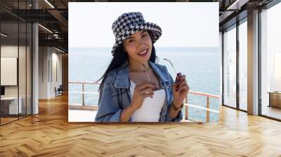 Beautiful asian woman holding black eyeglasses with hat on the sea Wall mural