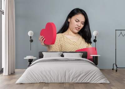 Young woman disappointed expression when opening heart shaped gift box Wall mural