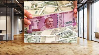 Close up view of woman's hands holding brand new indian 2000 rupees banknotes. 500 rupee banknotes in background. Wall mural