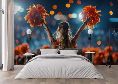 Energetic cheerleader with orange pom poms performing dance at sports event, back view Wall mural