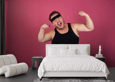 Funny fat man in a black T-shirt doing sports on a pink background. Fitness diet and weight loss. Wall mural