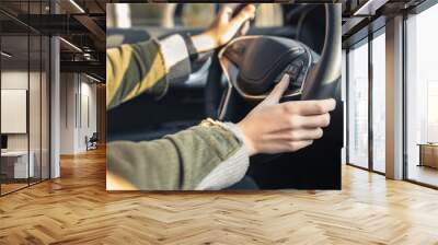 Young caucasian woman holding hands on steering wheel. By right hand she changing track or scrolls through the on-board computer menu. Driving car concept. Vehicle interior. Selective focus. Wall mural