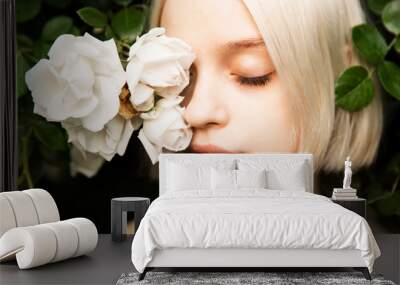 Portrait of beautiful young girl with closed eyes in white roses. Blond platinum girl with fair complexion and roses in front of her face Wall mural