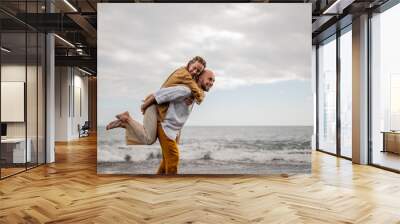 Playful young loving couple on a beach, man holding a girl in the air on his back Wall mural