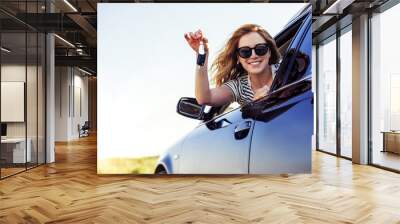 An attractive woman in a car holds a car key in her hand. Wall mural