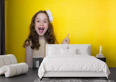 smiling little girl on yellow background points her finger at the space for lettering. Concept of education Wall mural