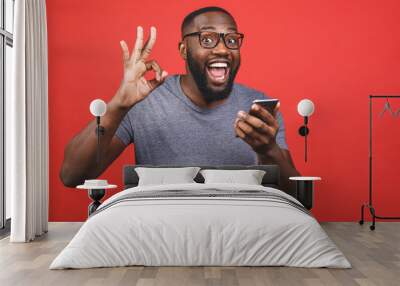 Afro american man using smartphone over isolated red background doing ok sign with fingers, excellent symbol. Wall mural