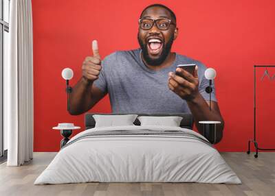 Afro american man using smartphone over isolated red background happy with big smile doing ok sign, thumb up with fingers, excellent sign. Wall mural