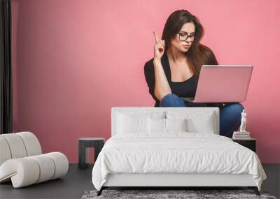 Business concept. Portrait of happy woman in casual sitting on floor in lotus pose and holding laptop isolated over pink background Wall mural