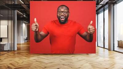 Closeup portrait of happy young handsome man looking shocked surprised open mouth eyes, isolated on red background. Positive human emotion facial expression feeling. Thumbs up. Wall mural