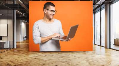 Confident business expert. Confident young handsome man in casual holding laptop and smiling while standing against orange background. Wall mural