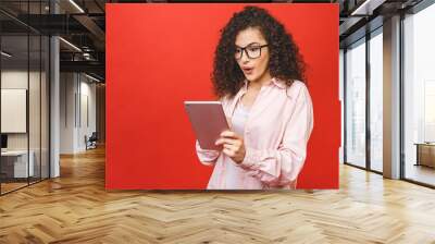 Excited amazed young beautiful woman with tablet pc. Happy girl in white shirt using tablet computer, isolated on red background. Wall mural