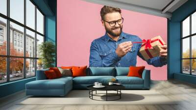 Happy holiday, my congredulations! Portrait of an attractive casual man giving present box and looking at camera isolated over pink background. Wall mural