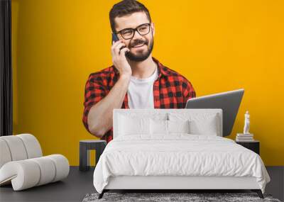 Happy smiling young business man in casual with a laptop sitting at floor calling with smart phone. Wall mural