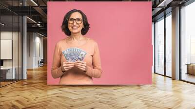 Happy winner! Image of a mature senior happy old woman standing isolated over pink background, holding money. Wall mural