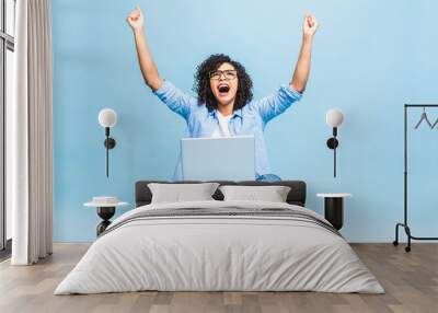 Happy winner. Portrait of african american black woman in casual sitting on floor in lotus pose and holding laptop isolated over blue background Wall mural