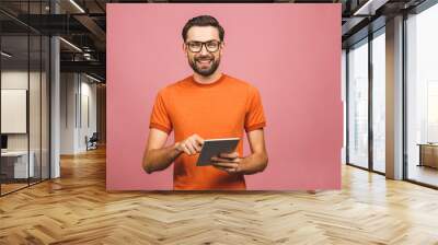 Happy young man in casual standing and using tablet isolated over pink background. Wall mural