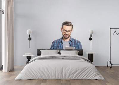 Happy young man in plaid shirt standing and using tablet over grey background Wall mural