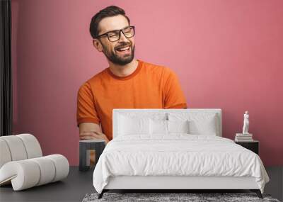 Happy young man. Portrait of handsome young man in casual keeping arms crossed and smiling while standing against pink background. Wall mural