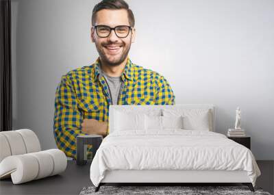 Happy young man. Portrait of handsome young man in casual shirt keeping arms crossed and smiling while standing against grey background Wall mural