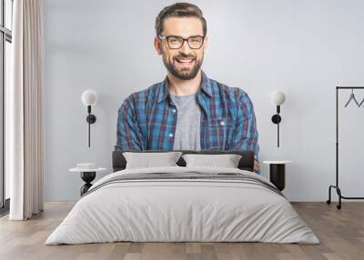 Happy young man. Portrait of handsome young man in casual shirt keeping arms crossed and smiling while standing against grey background Wall mural