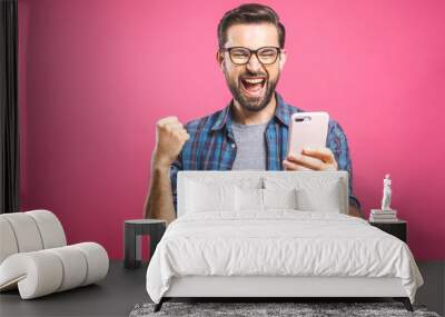 I'm a winner! Happy man holding smartphone and celebrating his success over pink background. Wall mural