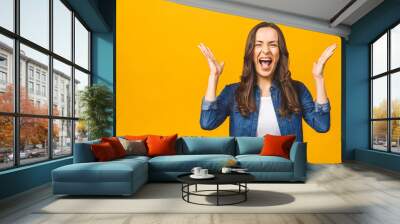 I'm winner! Happy successful young woman with raised hands shouting and celebrating success over yellow background. Wall mural