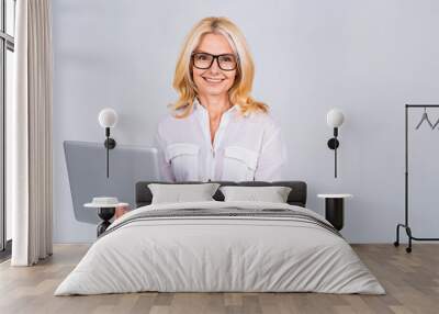 Image of cheerful mature business woman standing isolated over white background using laptop computer. Portrait of a smiling senior lady holding laptop computer. Wall mural