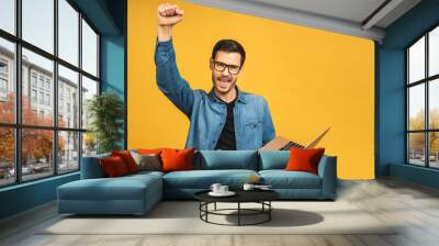 Image of happy excited young man posing isolated over yellow background wall using laptop computer make winner gesture. Wall mural