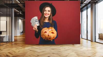 October sale! Halloween Witch with a carved Pumpkin and money - isolated on red background. Emotional young woman in Halloween costume. Halloween Party girl. Wall mural