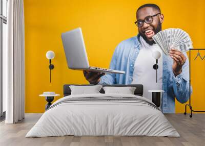 Photo of a happy young afro american handsome man posing isolated over yellow wall background using laptop computer holding money. Wall mural