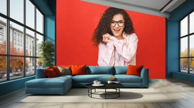 Photo of cheerful beautiful young woman standing isolated over red wall background. Looking camera showing winner gesture. Wall mural