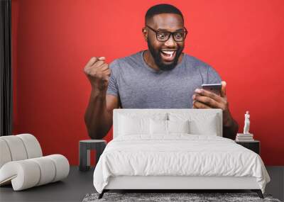 Photo of overjoyed black african american man knowing that he became winner of something so rejoicing enjoying news information while isolated over red background. Wall mural