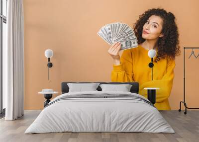 Portrait of a cheerful young woman holding money banknotes and celebrating isolated over beige background. Wall mural