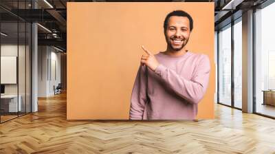 Portrait of a smiling happy african american black man in casual pointing with fingers aside isolated over beige background. Wall mural