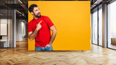 Portrait of an excited bearded happy man pointing finger up at copyspace isolated on yellow background. Copy space. Wall mural