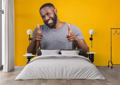 Portrait of cheerful, positive, handsome man with black skin, beaming smile in casual showing thumb up with finger to the camera isolated on yellow background. Wall mural