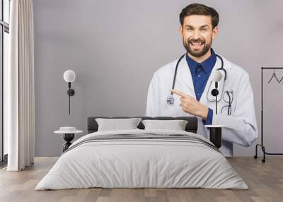 Portrait of cheerful smiling young doctor with stethoscope over neck in medical coat standing against isolated gray background. Wall mural