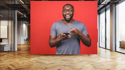 Portrait of handsome excited cheerful joyful delightful african american guy wearing casual sending and getting messages to his lover isolated against red background. Using phone. Wall mural