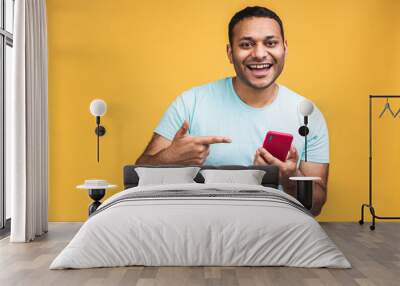 Portrait of handsome excited cheerful joyful indian african american guy wearing casual sending and getting messages to his lover isolated over yellow background. Using phone. Wall mural