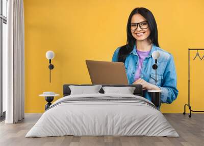 Portrait of happy young beautiful surprised woman with glasses standing with laptop isolated on yellow background. Space for text. Wall mural