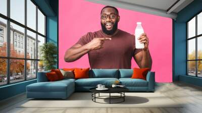 Portrait of young african american black man holding bottle of milk isolated over pink background. Healthy food concept. Wall mural