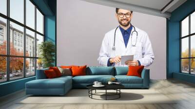 Smiling doctor using a tablet computer isolated on a grey background. Wall mural