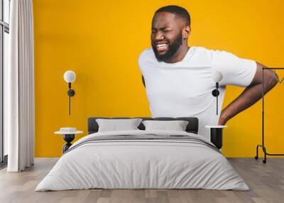 Young afro american young man suffering from backache for having made an effort on isolated background. Wall mural