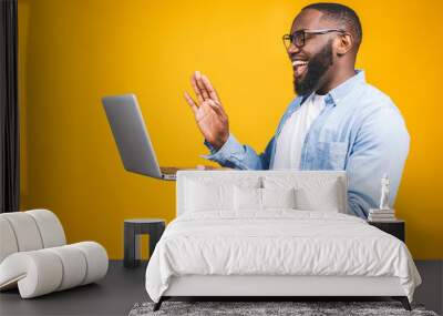 Young happy smiling african american man standing and using laptop computer isolated over yellow background. Wall mural