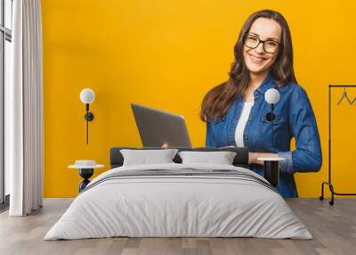 Young happy smiling woman in casual clothes holding laptop and sending email to her best friend. Isolated against yellow background. Wall mural